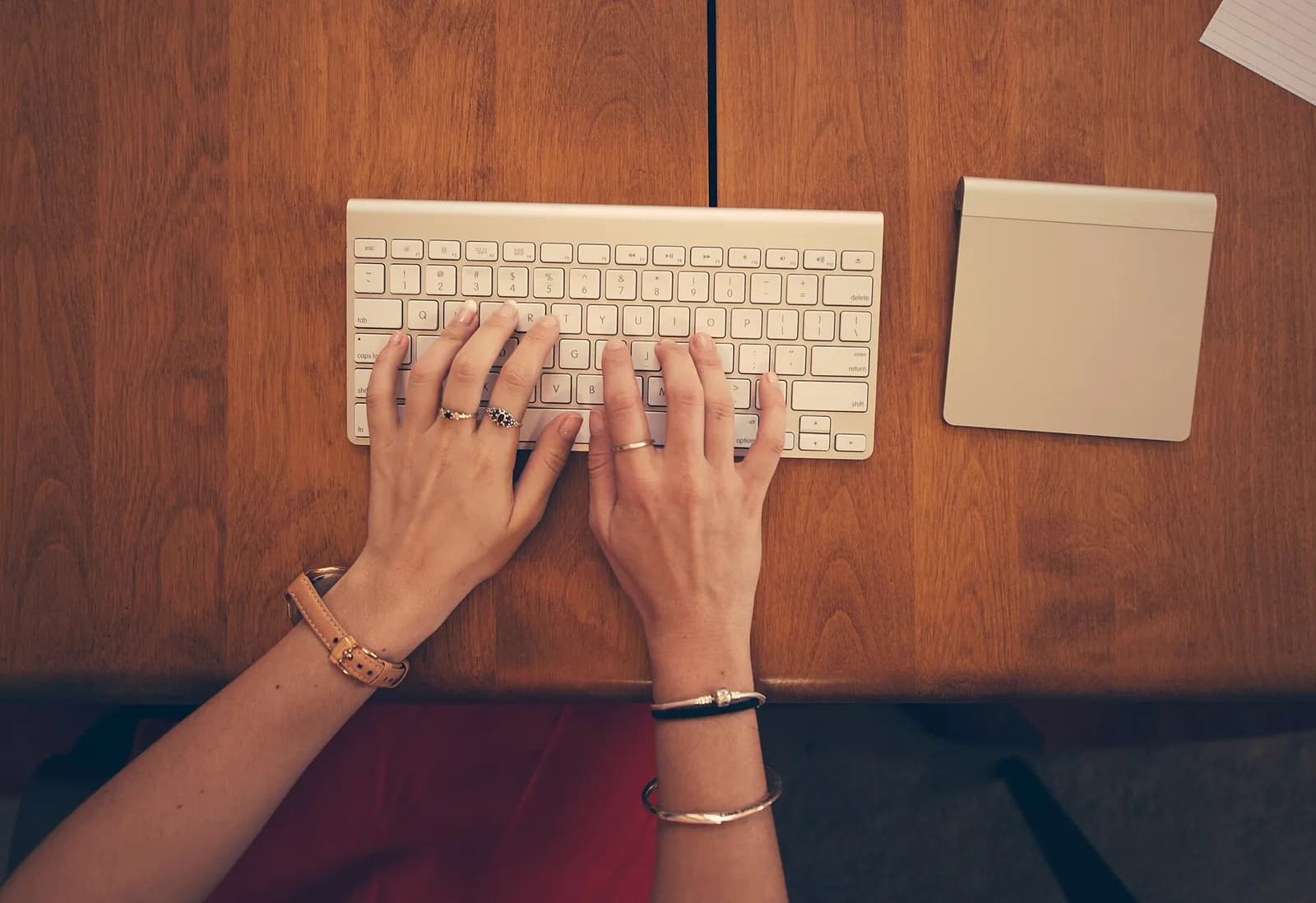 Hands typing on a white wireless keyboard on a wooden desk, seen from above