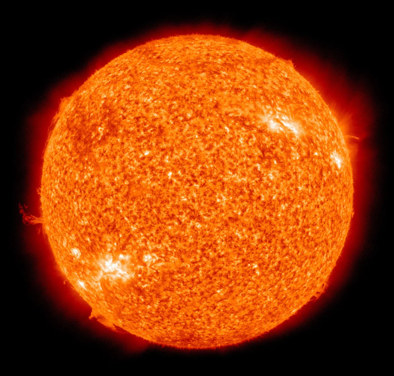 El Sol en luz ultravioleta extrema con colores falsos, visto por el Solar Dynamics Observatory de la NASA: un disco naranja de superficie granulada, con zonas brillantes y arcos de gas en el borde, sobre negro