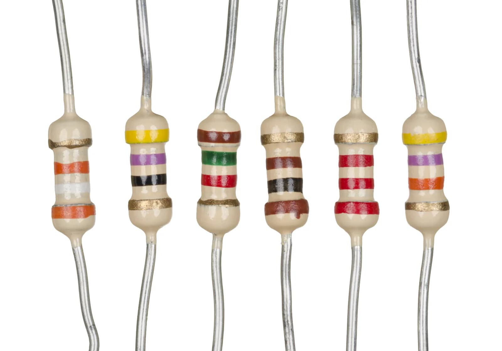 Six axial-lead resistors lying in a row on a white surface, with coloured bands that encode their different resistances