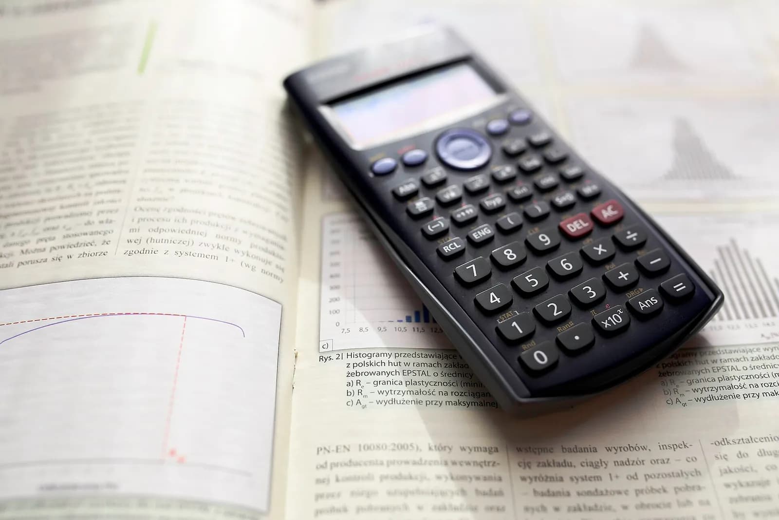 A black scientific calculator lying on an open textbook with histograms and printed text