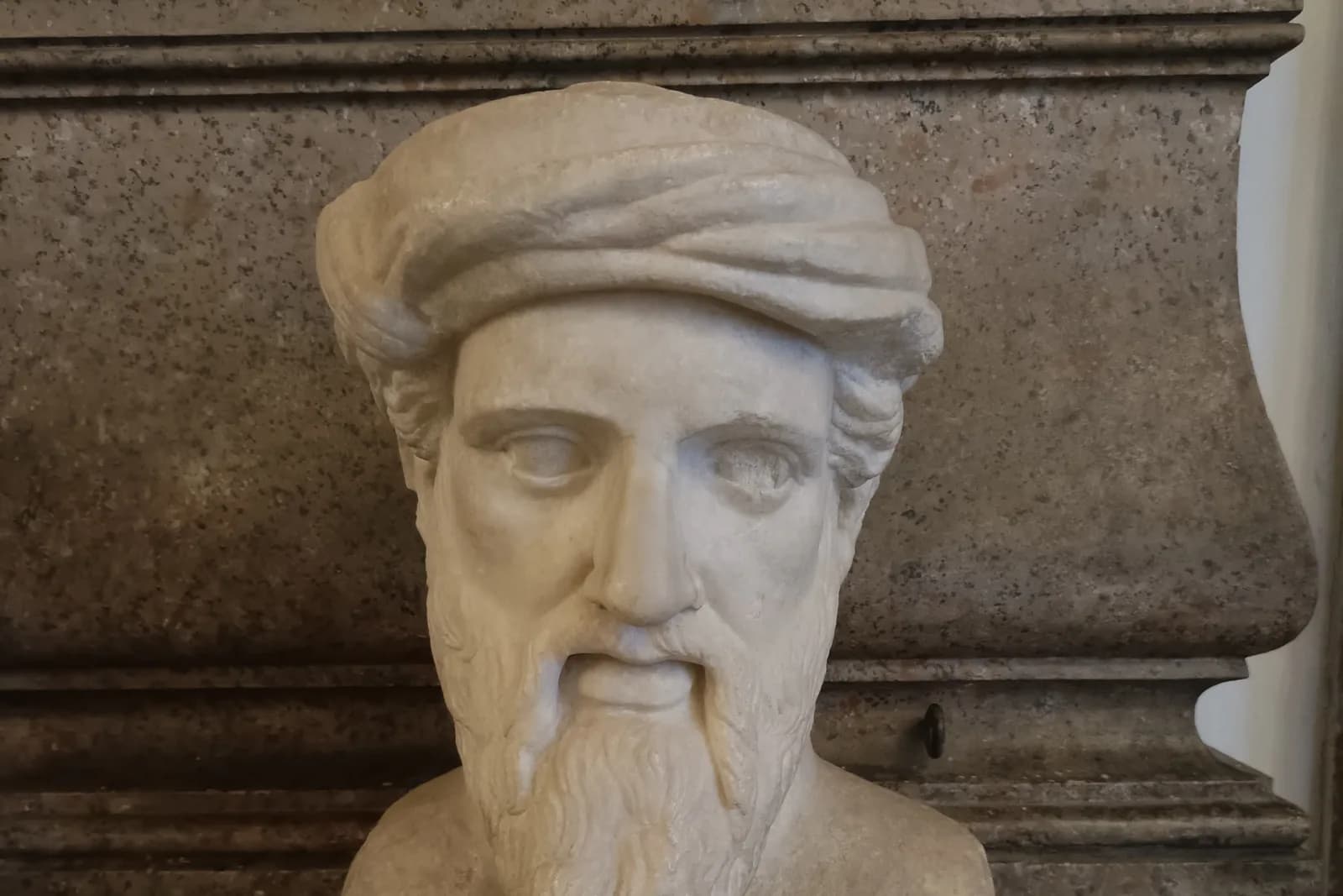 Roman marble bust of Pythagoras in the Capitoline Museums: a bearded man in a twisted cap against a granite wall