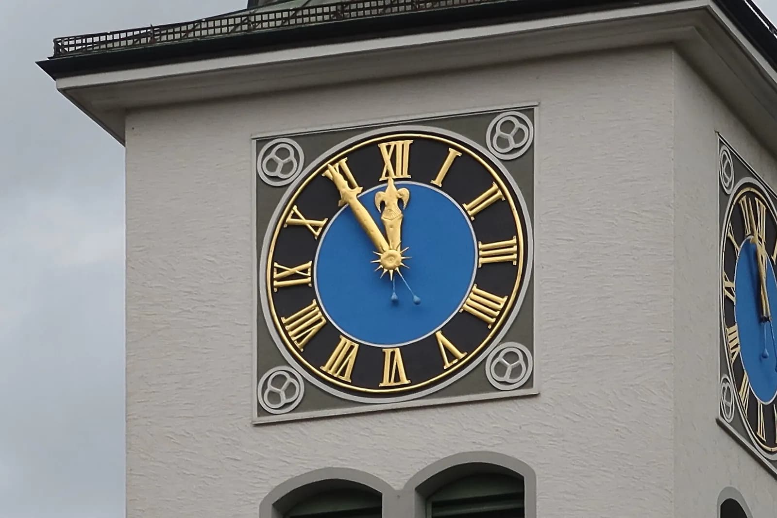 A tower clock with gold Roman numerals on a black ring and a blue centre, with four o'clock written IIII and nine o'clock IX