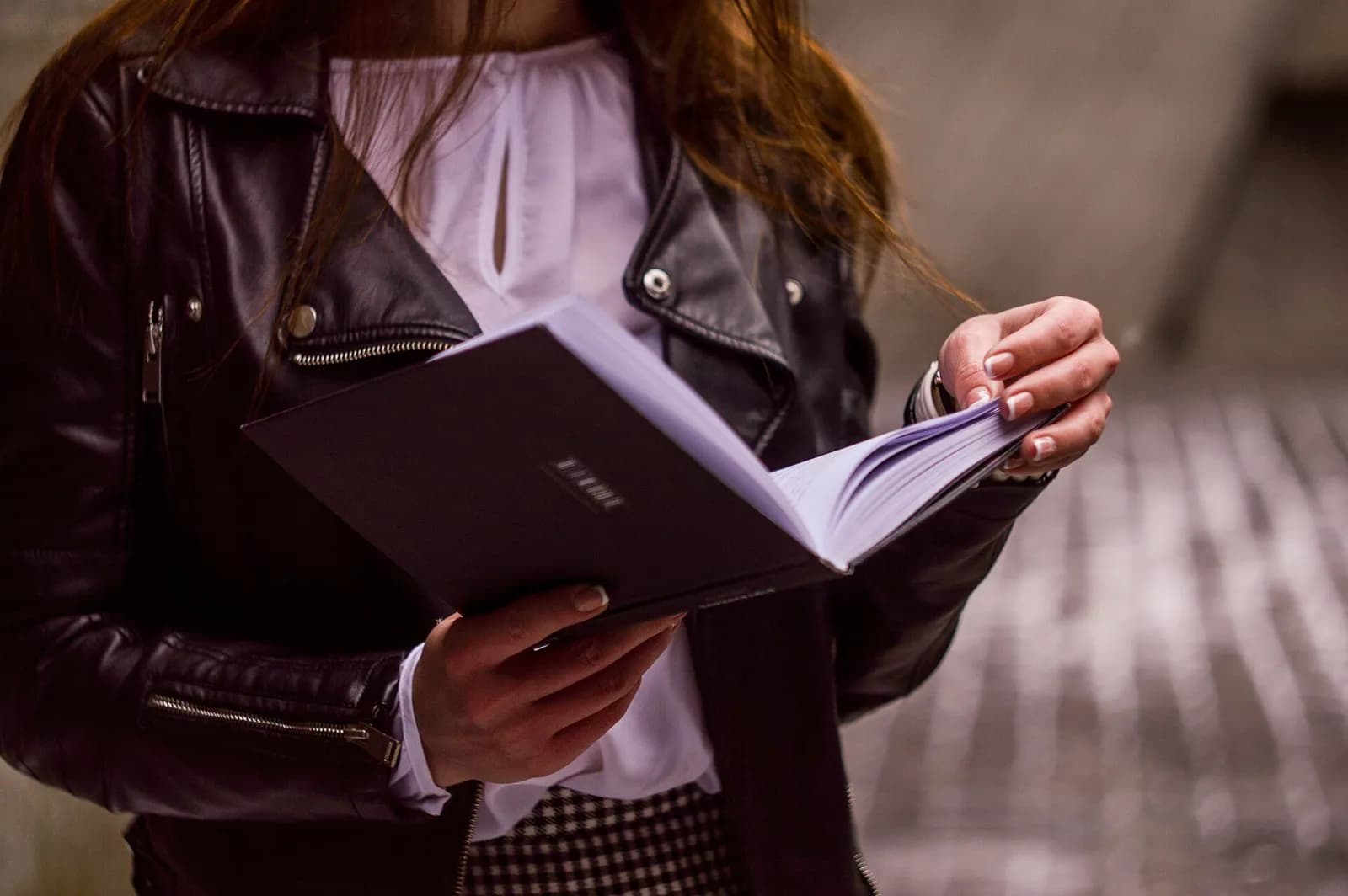 A woman in a black leather jacket leafing through an open book, her face out of frame