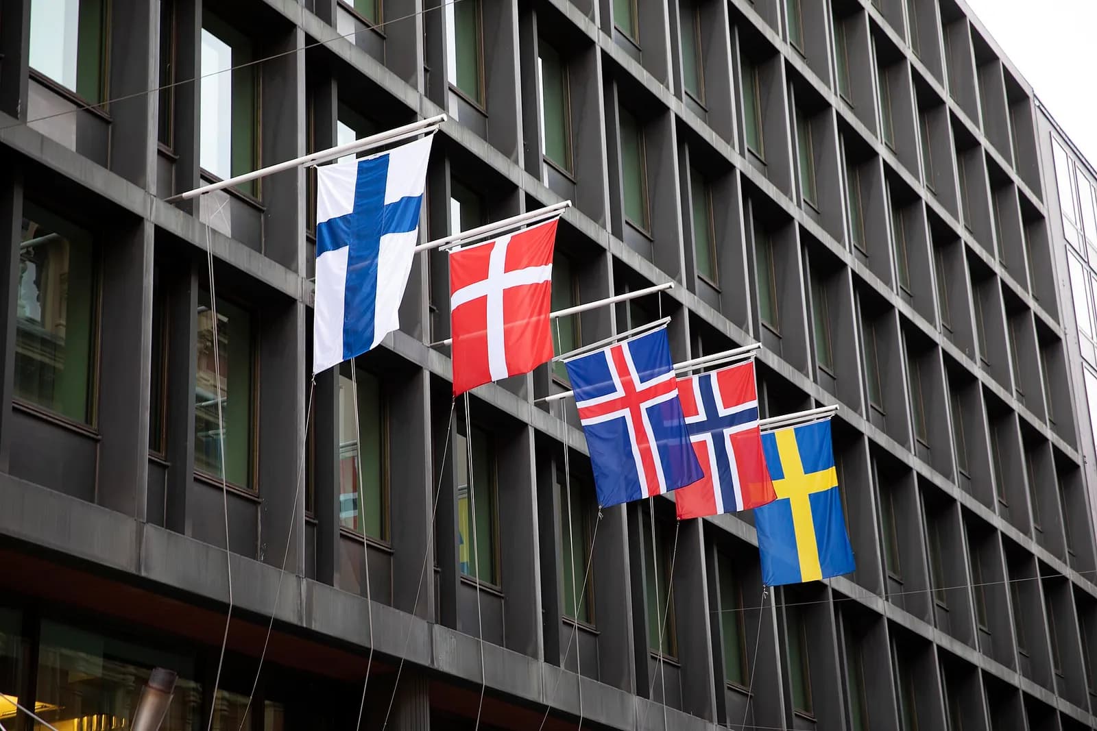 The flags of Finland, Denmark, Iceland, Norway and Sweden, all with Nordic crosses, hanging in a row from poles on a dark office facade in Helsinki