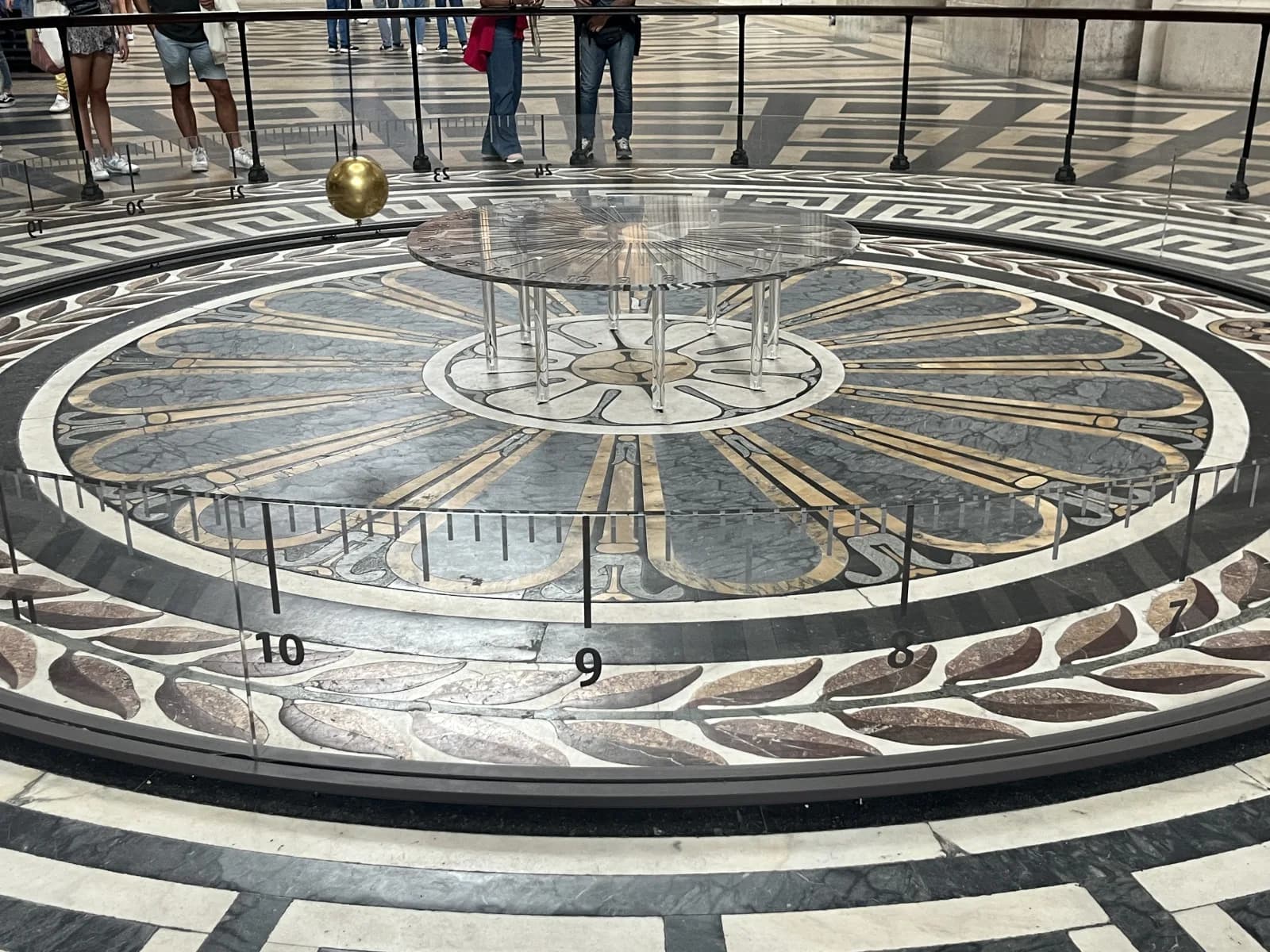 The golden bob of the Foucault pendulum hanging over the circular marble floor of the Panthéon in Paris, with a numbered scale around it
