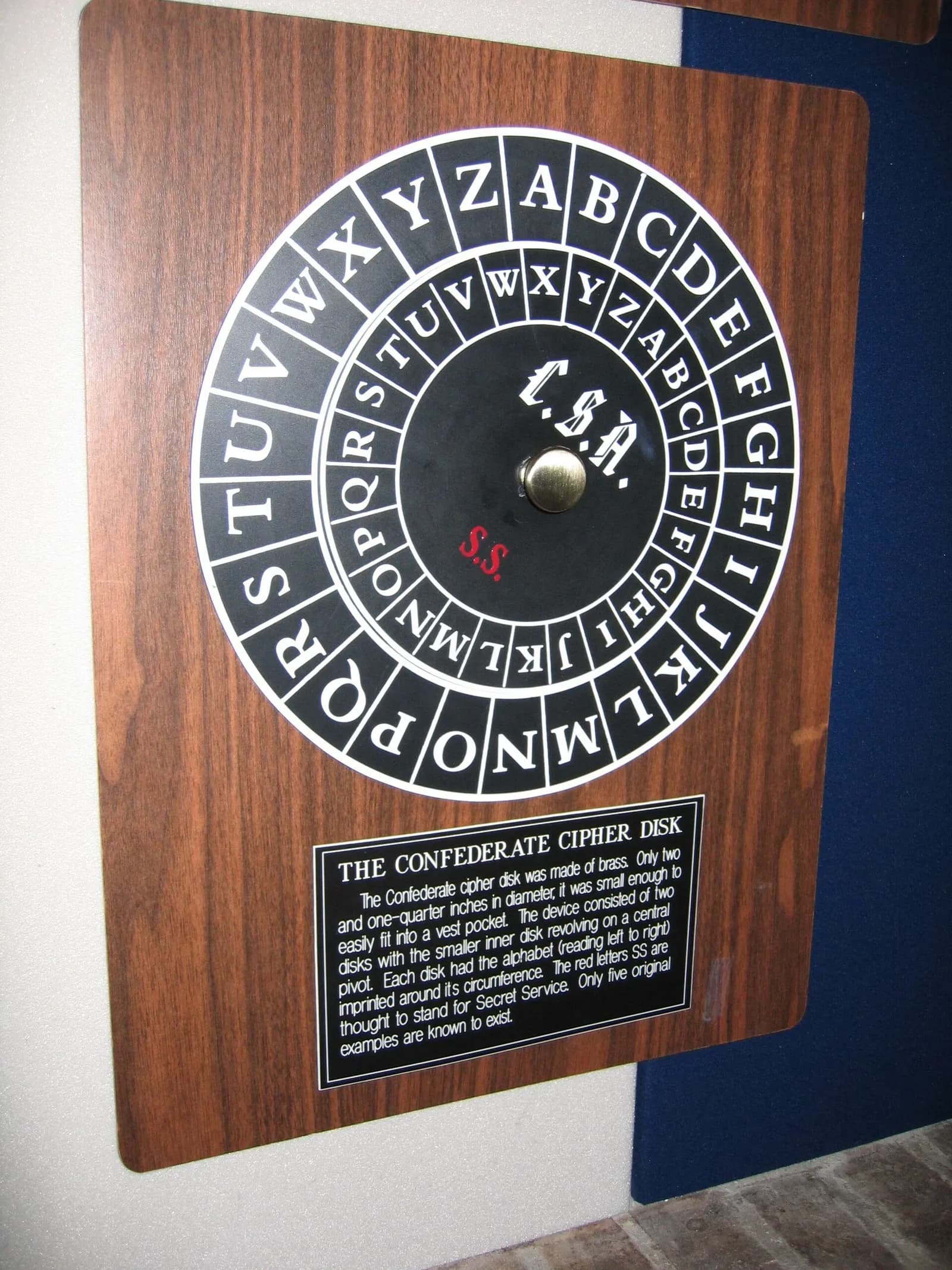 An enlarged reproduction of the Confederate cipher disk on a wooden museum panel: two black rings of white capital letters, the inner alphabet turned against the outer one, marked C.S.A., with a caption plaque below