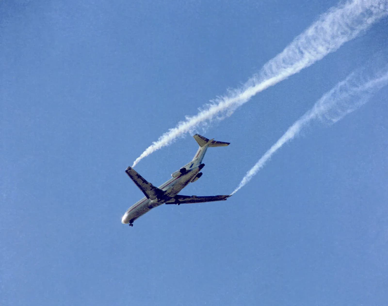 A Boeing 727 banking in a blue sky, with two white smoke trails from its wingtips curling into the swirling air behind the wings
