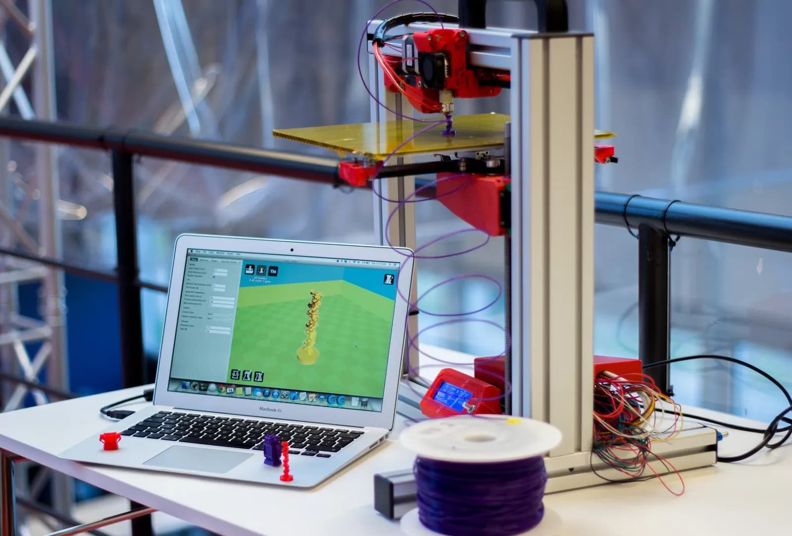 Une imprimante 3D sur une table à côté d’un ordinateur portable affichant un modèle 3D et d’une bobine de filament