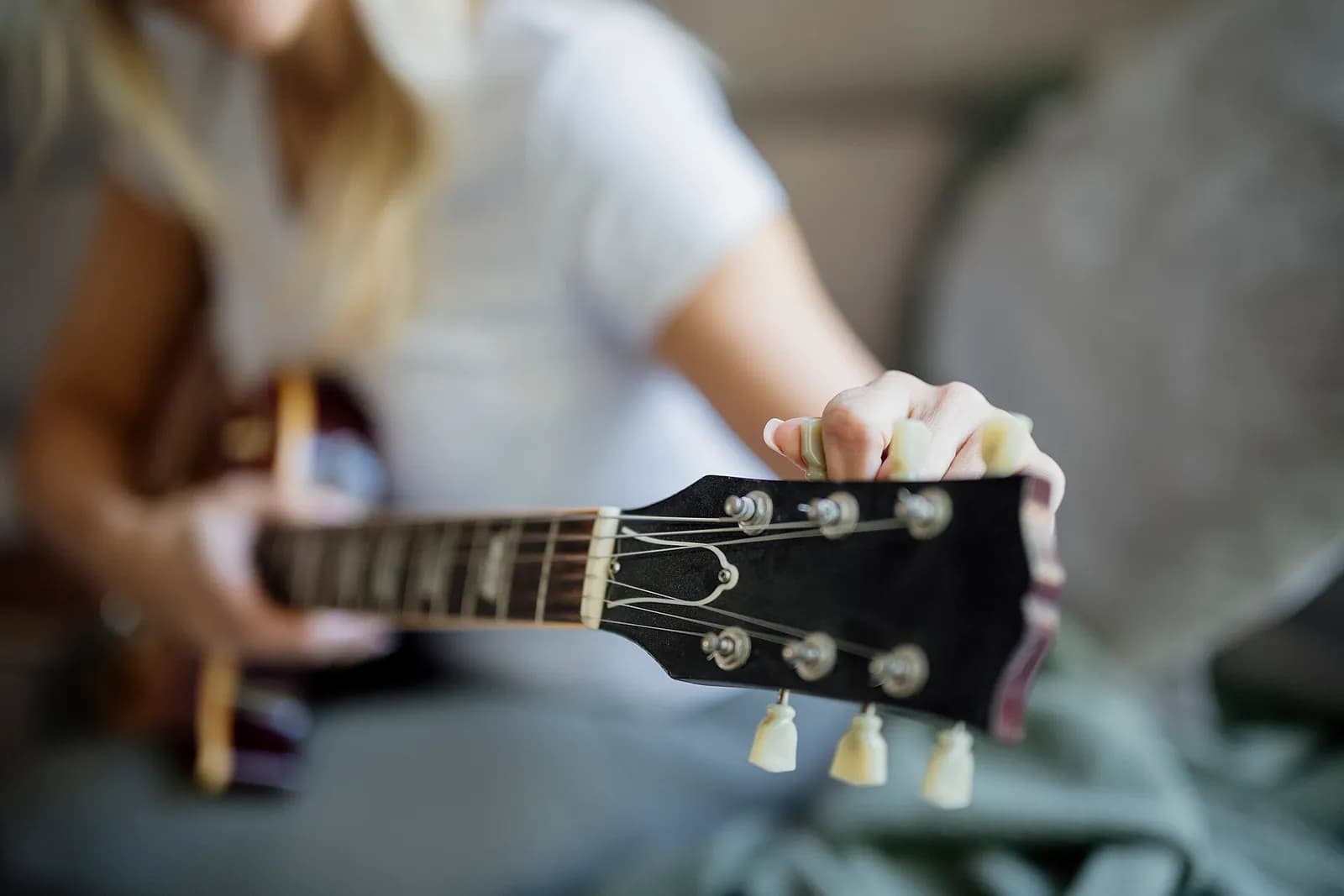 A hand turning a tuning peg on the headstock of an electric guitar, the player blurred in the background