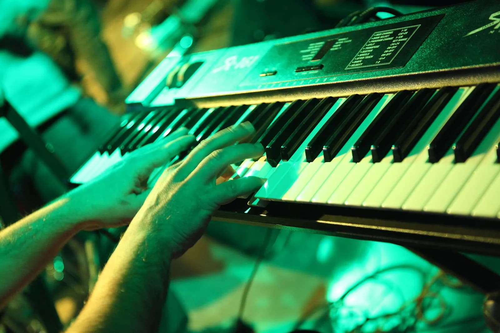 Two hands playing chords on a black electronic keyboard under green stage light