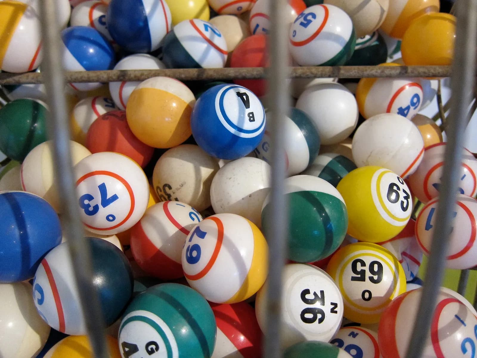 Numbered bingo balls in many colours piled up inside a wire drum