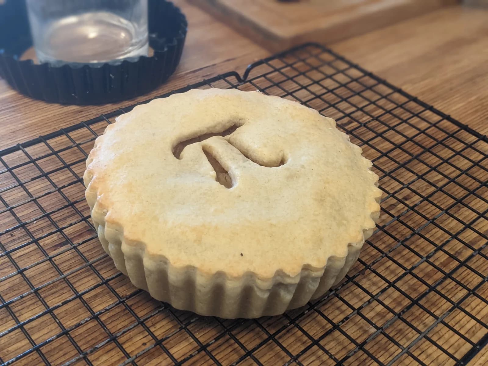 A round baked pie on a cooling rack with the Greek letter pi cut into its crust